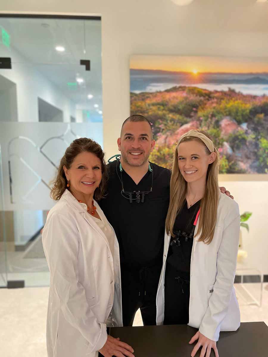 “Dr. Rima Shahhal (left), Dr. Sami Shahhal (center), and Dr. Ashley Ingram (right) standing in the Nordahl Dental office lobby, smiling in scrubs and white coats.”